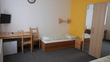 Cozy retreat with a single bed, desk, and chair, featuring a television and small refrigerator.
