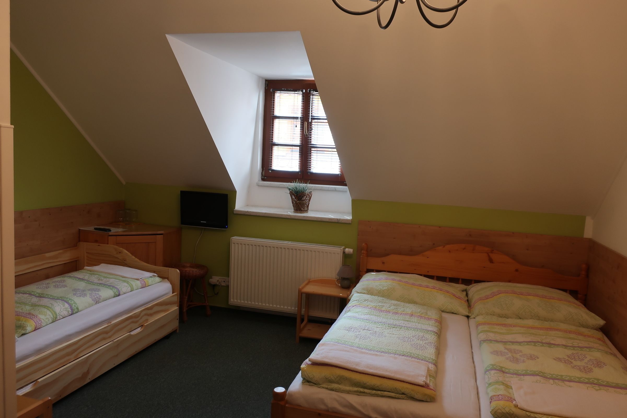 A small, cozy attic bedroom with two wooden beds, a window with a view, and a radiator.