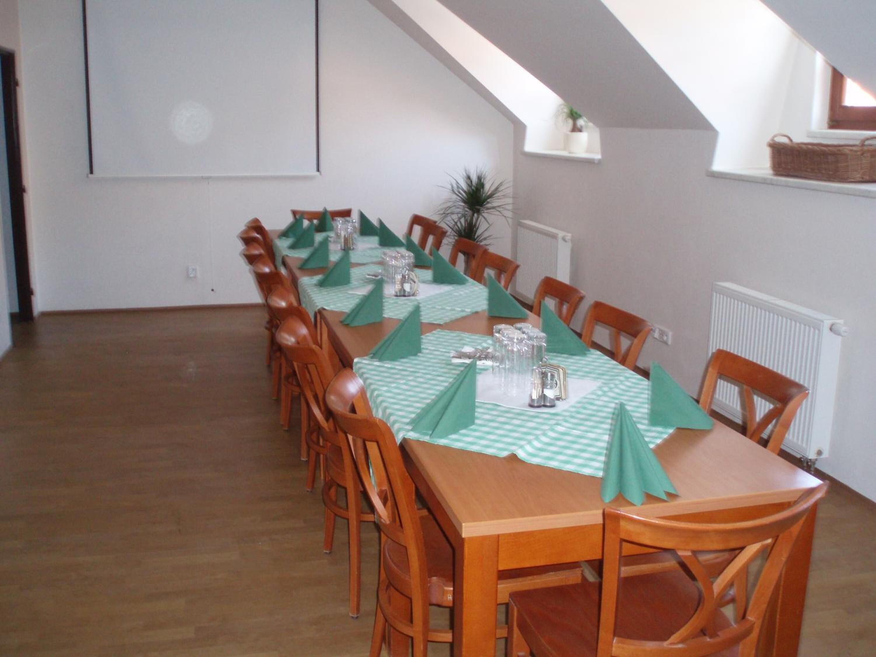 A long dining table with green tablecloths and wooden chairs, set in a room with a sloped ceiling and a radiator.