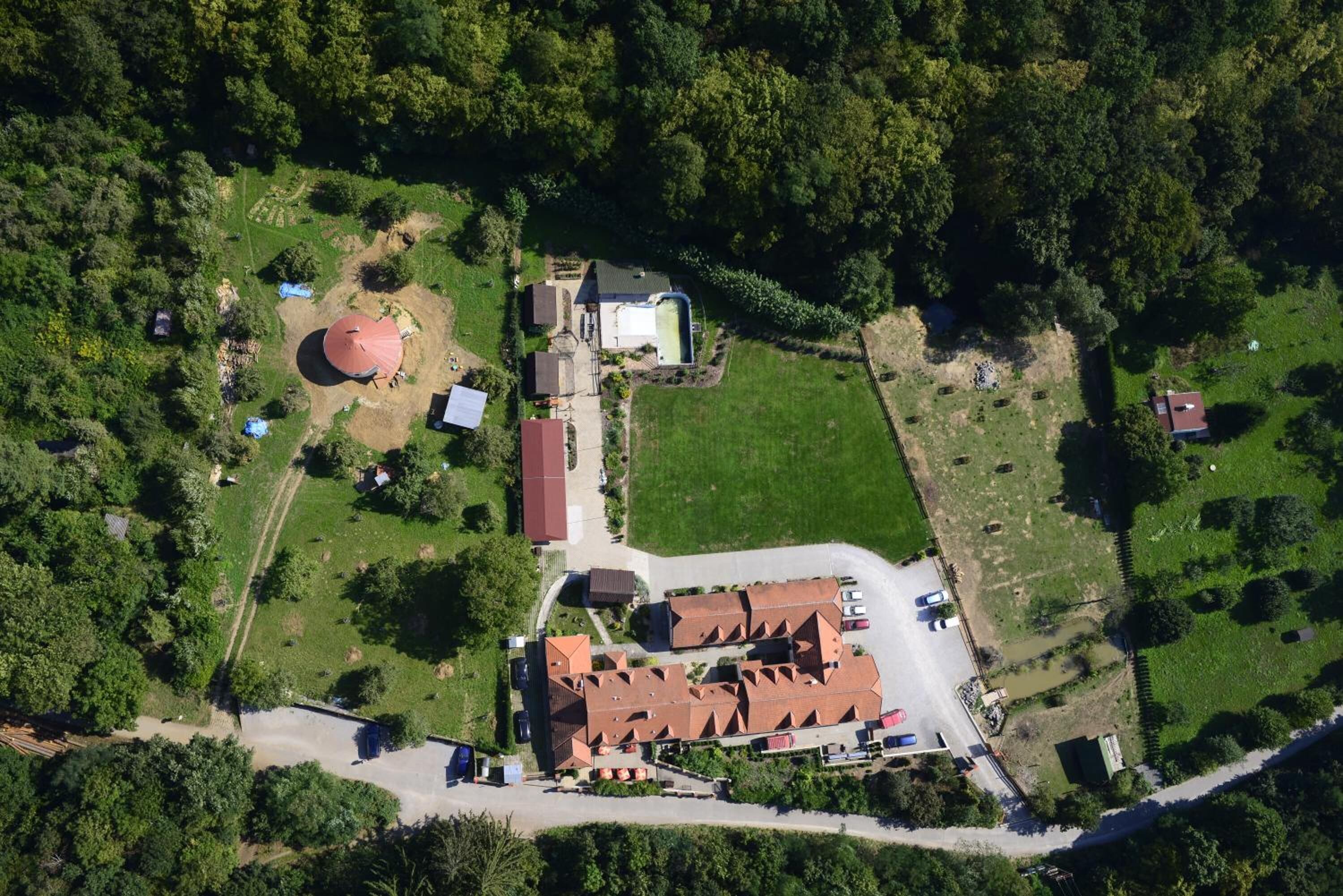 An aerial view of a property with a large building with a red roof, a circular structure, and a fenced area.
