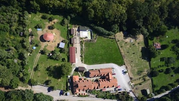 An aerial view of a property with a large building with a red roof, a circular structure, and a fenced area.