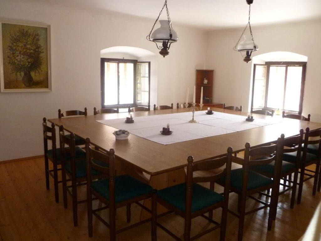 A dining room with a large wooden table, six chairs, two hanging lamps, and a painting on the wall.