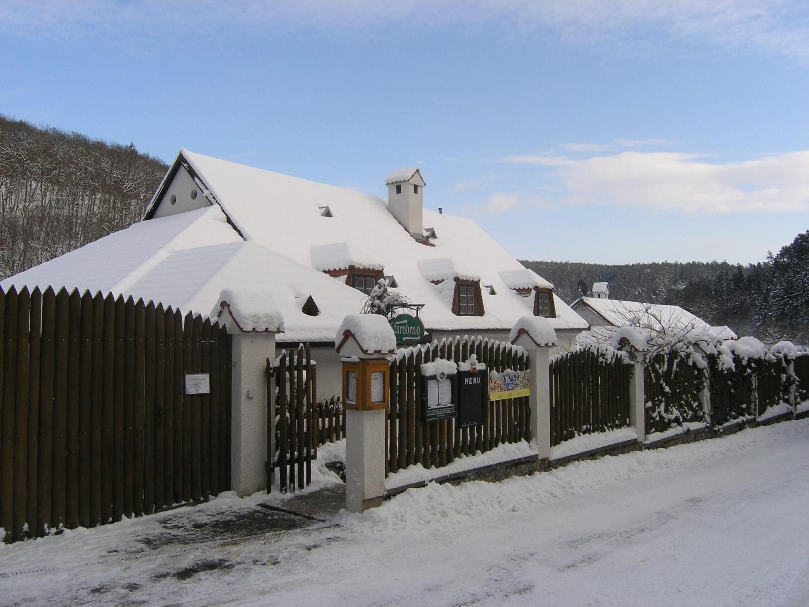 En snötäckt byggnad med ett staket av trä, en skylt och en menytavla.