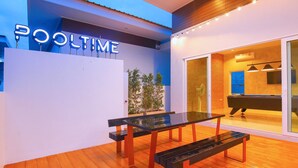 Uma área à beira da piscina com mesa de bilhar, bancos e uma placa com a inscrição 'POOLTIME'.