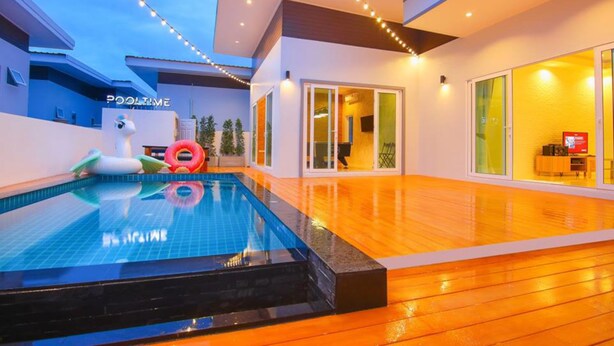 Uma área de piscina moderna com piscina transparente, deck de madeira e luzes de corda.