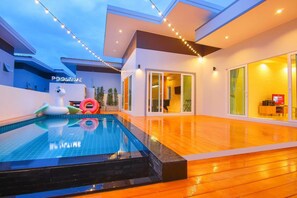 Un espace piscine moderne avec une piscine à eau claire, une terrasse en bois et des guirlandes lumineuses.