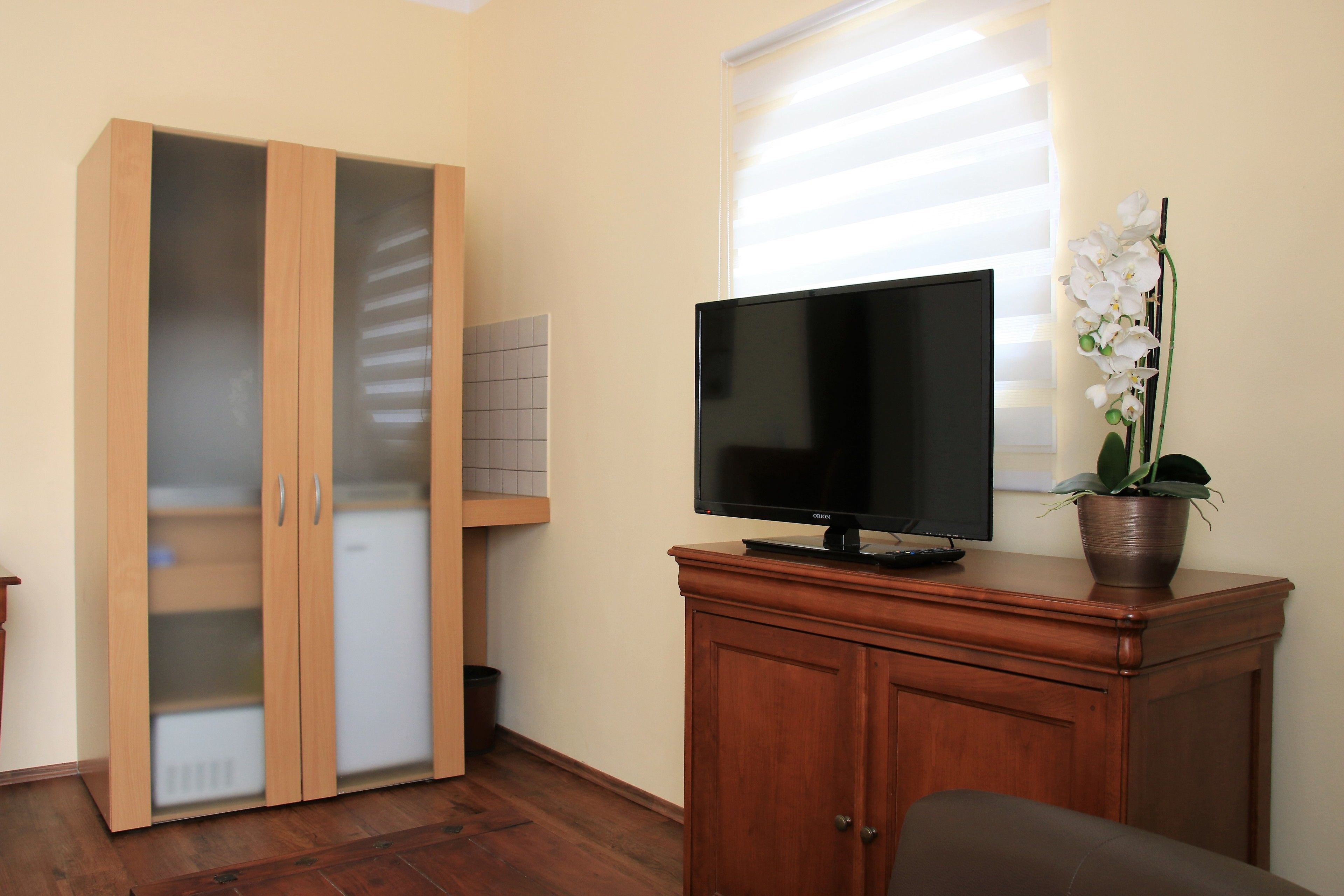 A room with a wardrobe, a television on a cabinet, and a window with blinds.
