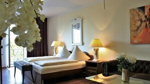 A hotel room with a bed, two bedside tables with lamps, a sofa, a glass coffee table, and a painting on the wall. - Apart Hotel Scheuer (Huerth)
