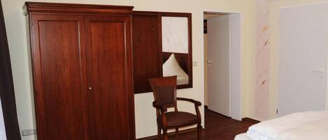 A bedroom with a wooden wardrobe, a chair, a bed, and a door.