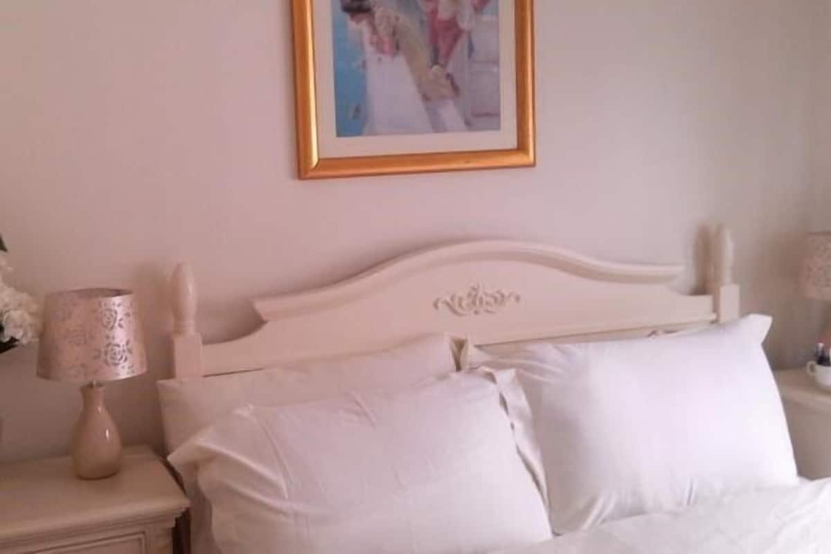 A bedroom with a white bed, a nightstand with a lamp, and a framed picture on the wall.