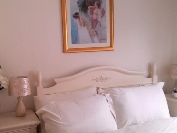 A bedroom with a white bed, a nightstand with a lamp, and a framed picture on the wall.
