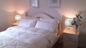 A neatly made bed with white linens, two bedside lamps, and a vase with flowers on a nightstand. - The Vee B&B (Waterford)