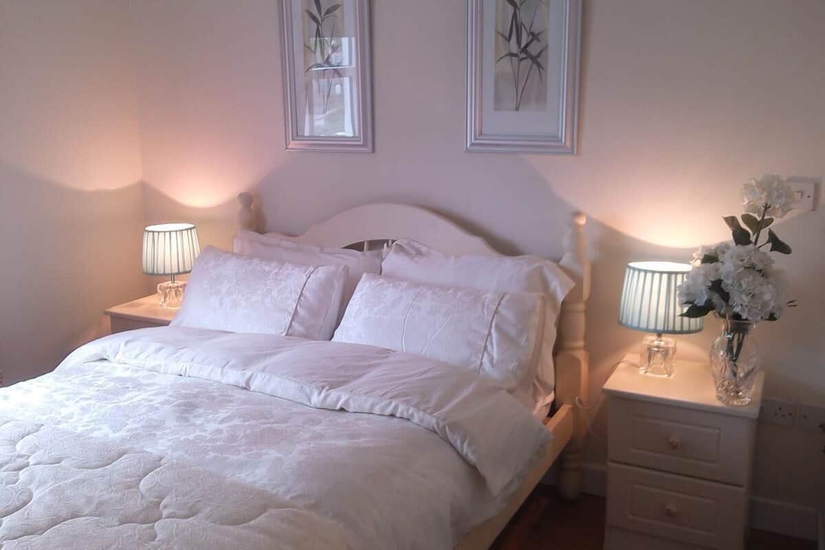 A neatly made bed with white linens, two bedside lamps, and a vase with flowers on a nightstand.