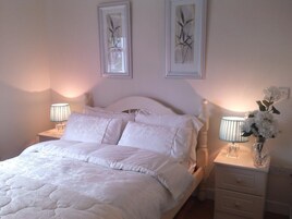 A neatly made bed with white linens, two bedside lamps, and a vase with flowers on a nightstand.