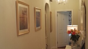 A hallway with framed artwork on the walls, a door with the number 5, and a lamp with flowers on a table. - The Vee B&B (Waterford)