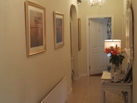 A hallway with framed artwork on the walls, a door with the number 5, and a lamp with flowers on a table.