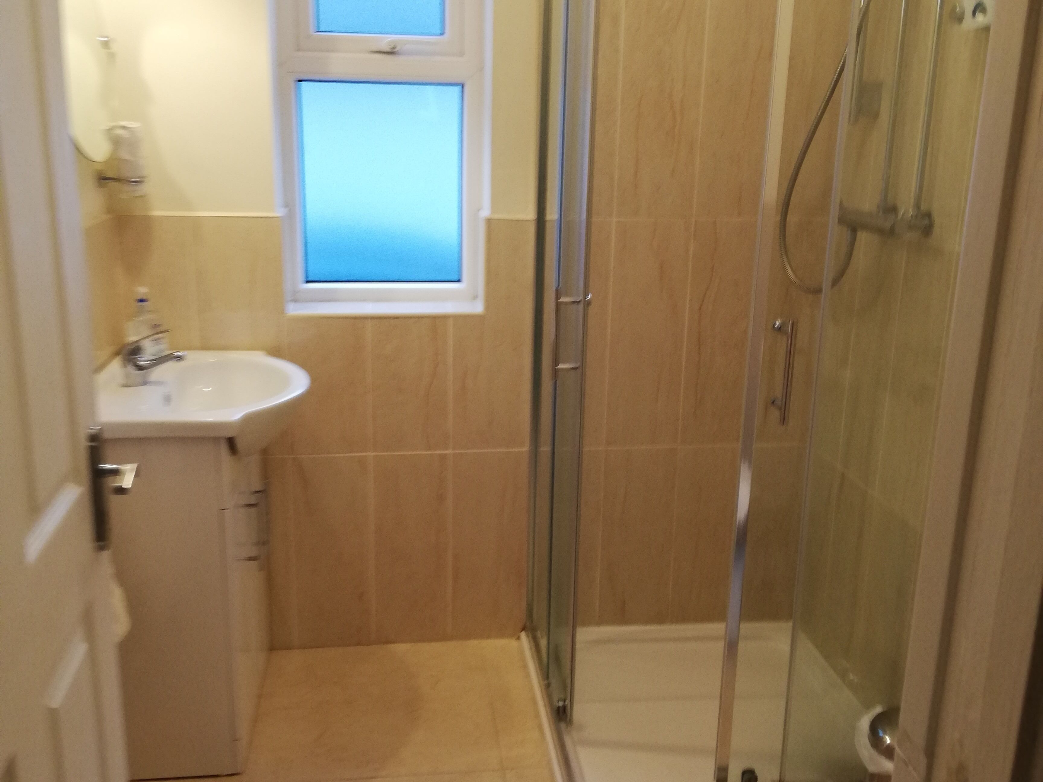A small bathroom with a sink, a window, and a glass shower enclosure.