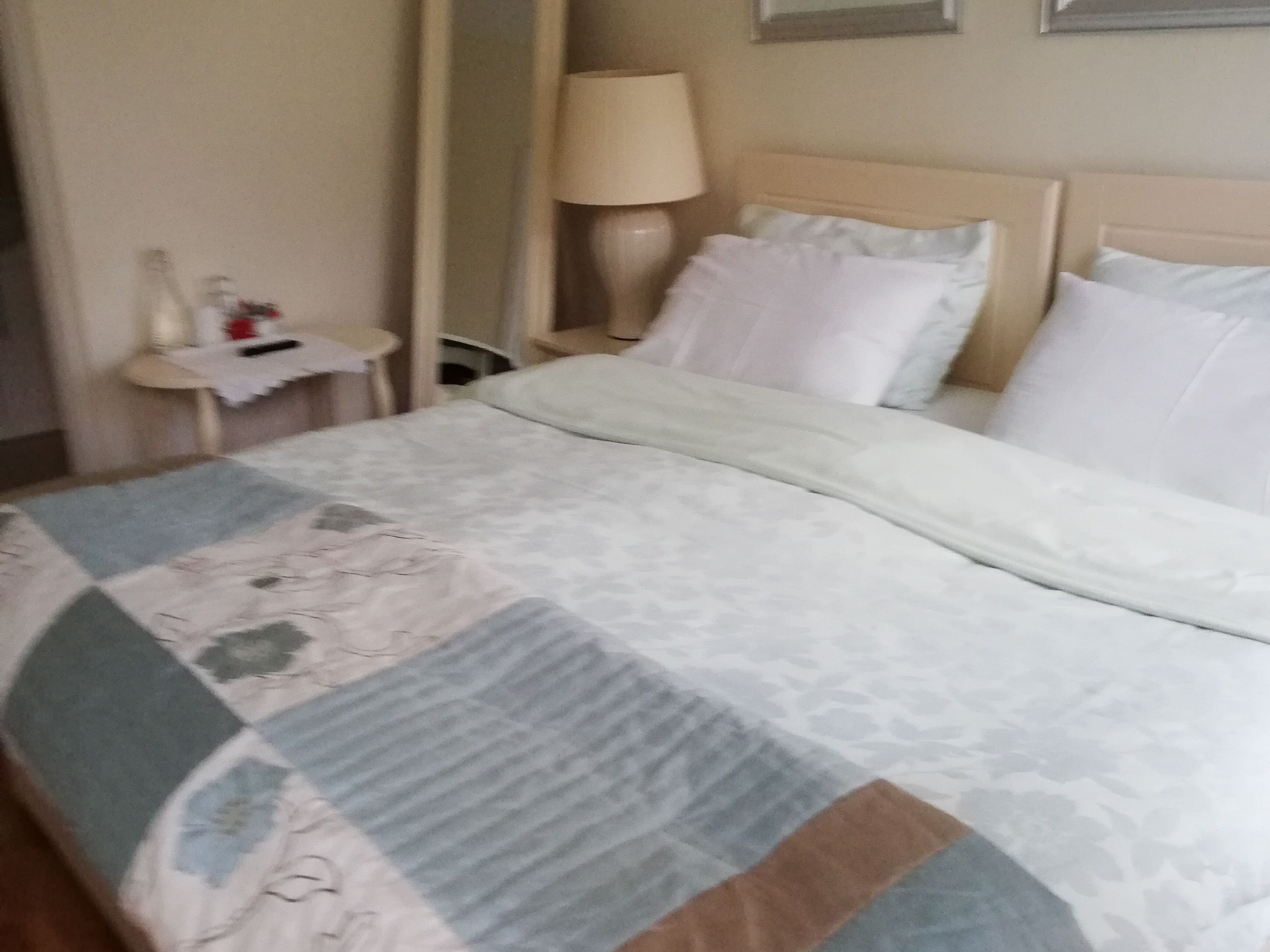 Habitación de hotel con cama, mesita de noche, lámpara y una pequeña mesa con una botella y un vaso.