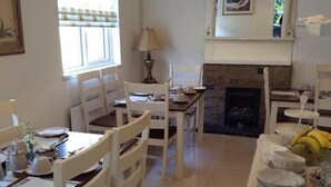 A dining area with white wooden chairs and tables, a fireplace, and a window with curtains. - The Vee B&B (Waterford)