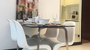 Un espace repas moderne avec une table en verre, des chaises blanches et un tableau décoratif au mur.