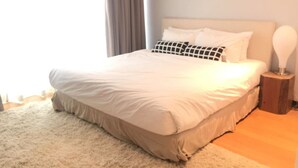Un lit bien fait, avec une couette blanche et beige, une table de chevet en bois avec une lampe, et un tableau accroché au mur.