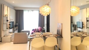 Un espace de salle à manger moderne, avec une grande table dressée pour quatre personnes, entourée de chaises blanches, et un lustre suspendu au-dessus.