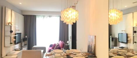 A modern dining area with a large table set for four, surrounded by white chairs, and a chandelier hanging above.
