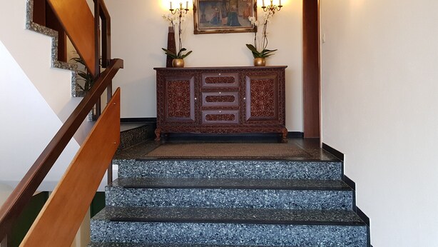 A staircase with a wooden handrail, a marble floor, a wooden cabinet with ornate carvings, and a framed painting above it. - Hotel Garni Elisabeth (Goeppingen)