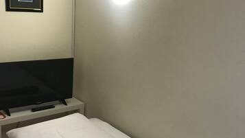 A single bed with a white mattress and a blanket, a flat-screen TV on a stand, a remote control, and a framed picture on the wall.