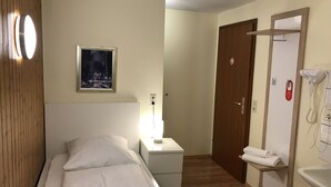 A hotel room with a bed, a nightstand, a mirror, a towel rack, and a wall-mounted phone. - Hotel Garni Elisabeth (Goeppingen)