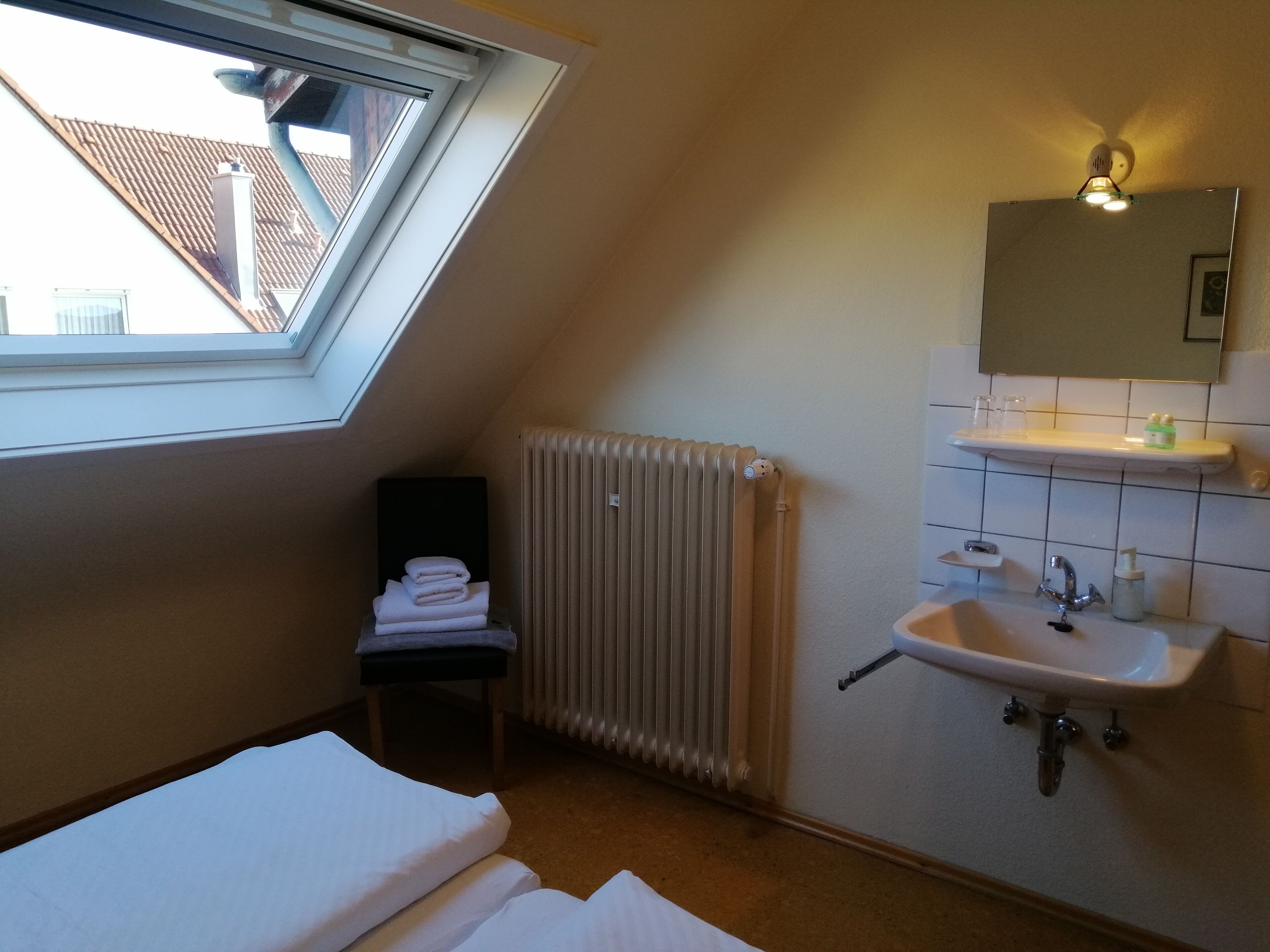Ein kleiner, gut beleuchteter Raum mit Dachfenster, Heizkörper, Spüle und Spiegel.