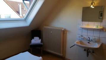 Ein kleiner, gut beleuchteter Raum mit Dachfenster, Heizkörper, Spüle und Spiegel.
