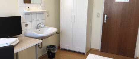 A small, clean room with a white sink, a mirror, a wardrobe, and a bed.
