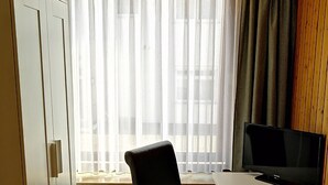 A room with a white desk, a black chair, a television on the desk, a radiator below the window, and a wardrobe to the left. - Hotel Garni Elisabeth (Goeppingen)