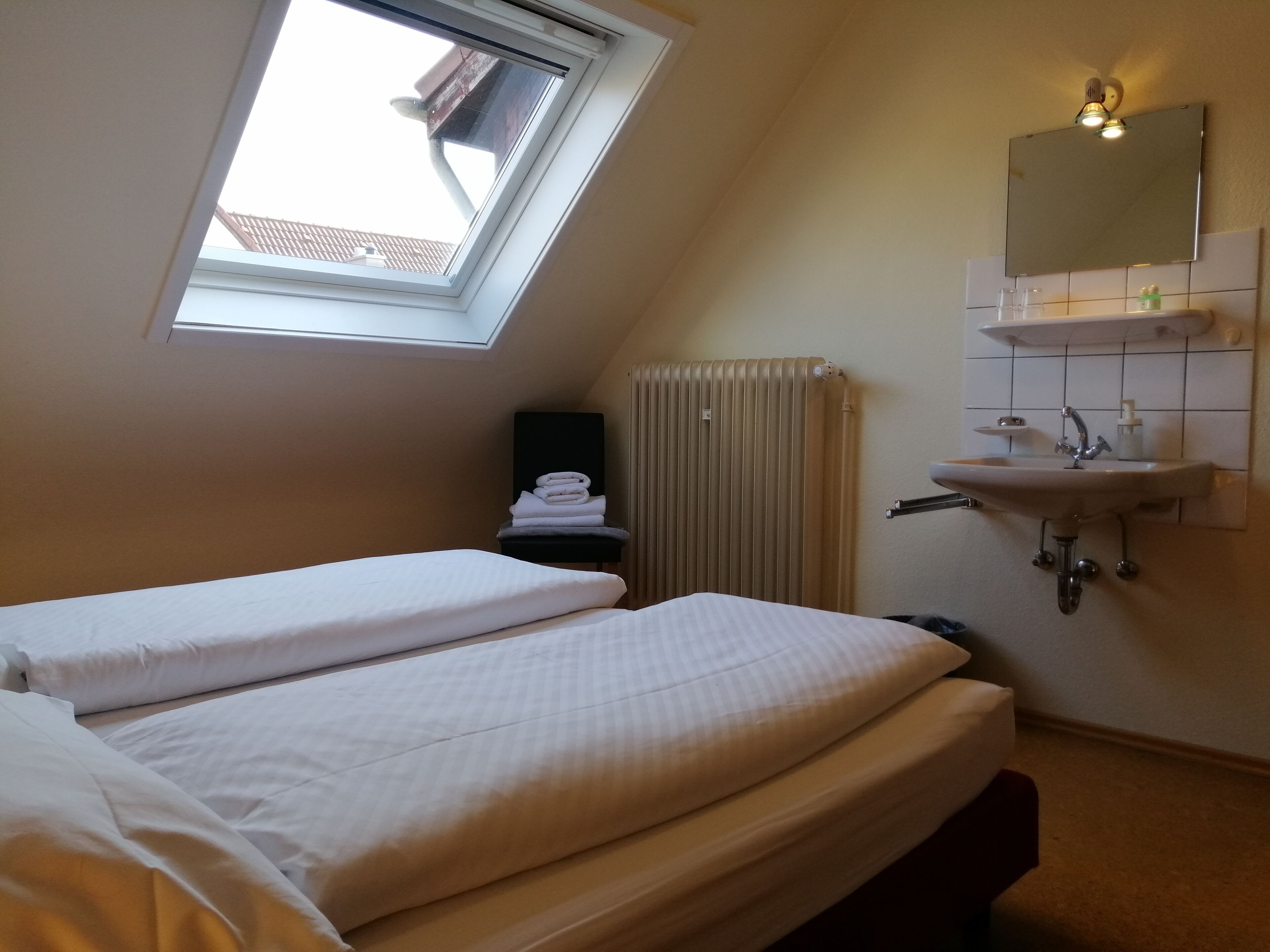 Une chambre avec deux lits, une lucarne, un radiateur, un lavabo et un miroir.