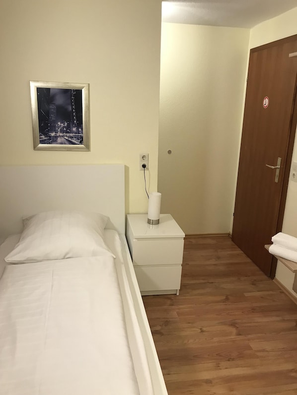 A bedroom with a bed, a nightstand with a lamp, a wall-mounted picture, and a door. - Hotel Garni Elisabeth (Goeppingen)