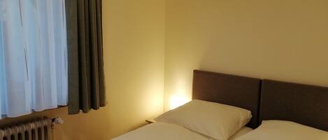 A hotel room with a bed, a nightstand, a lamp, and a window with curtains.