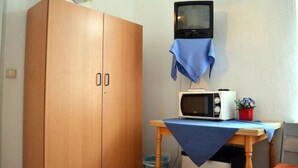 A room with a wooden wardrobe, a table with a microwave, a television, and a small plant. - Pension Dessauer Hof (Halle (Saale))