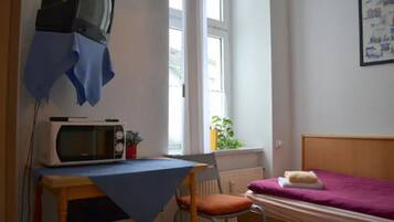 A small room with a bed, a table with a microwave, a chair, and a television on the wall.