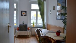 A room with a bed, a table with a chair, a television on a small table, and a window with a curtain. - Pension Dessauer Hof (Halle (Saale))