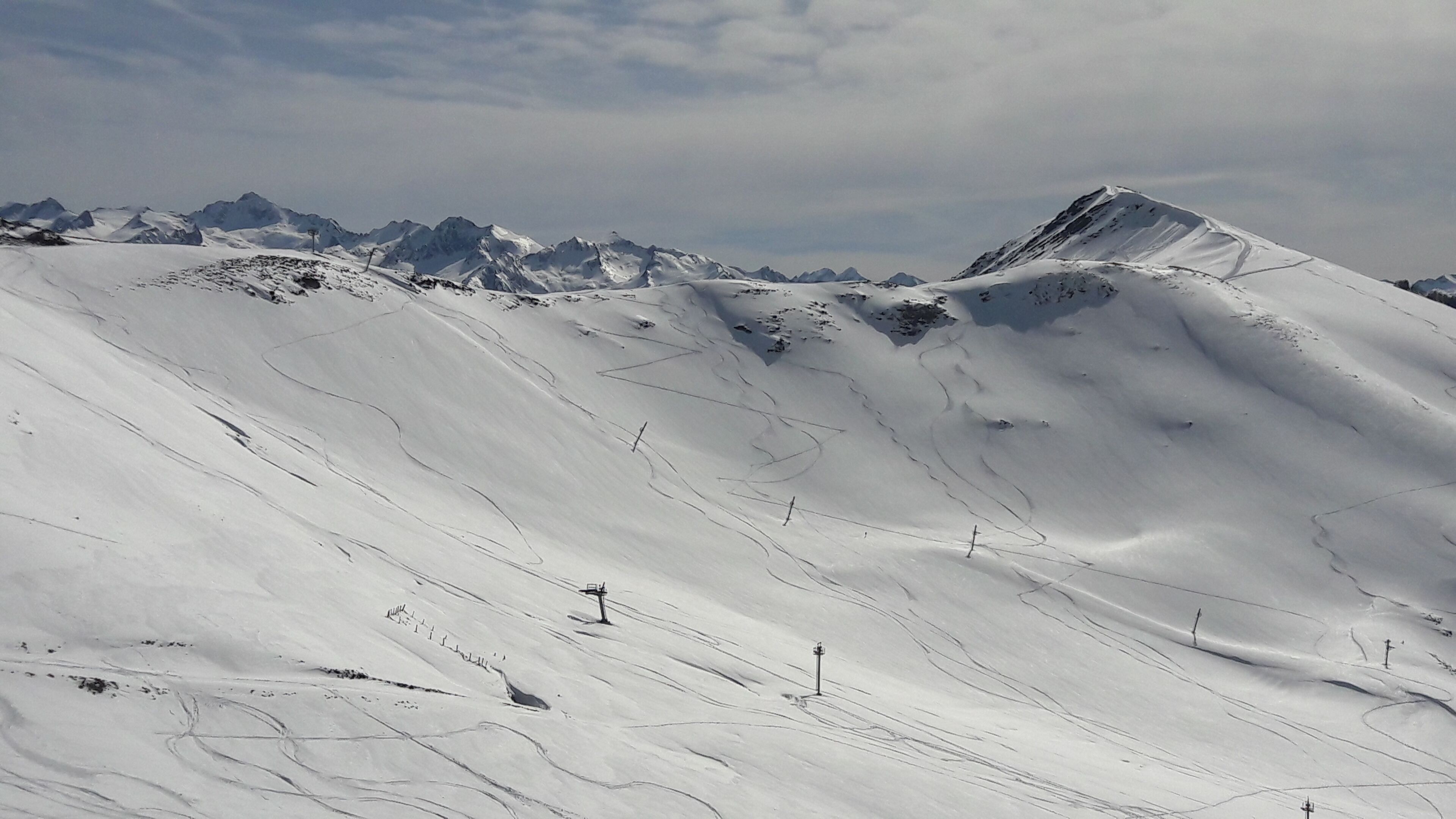 A snow-covered mountain landscape with ski tracks and poles, indicating a ski resort area.