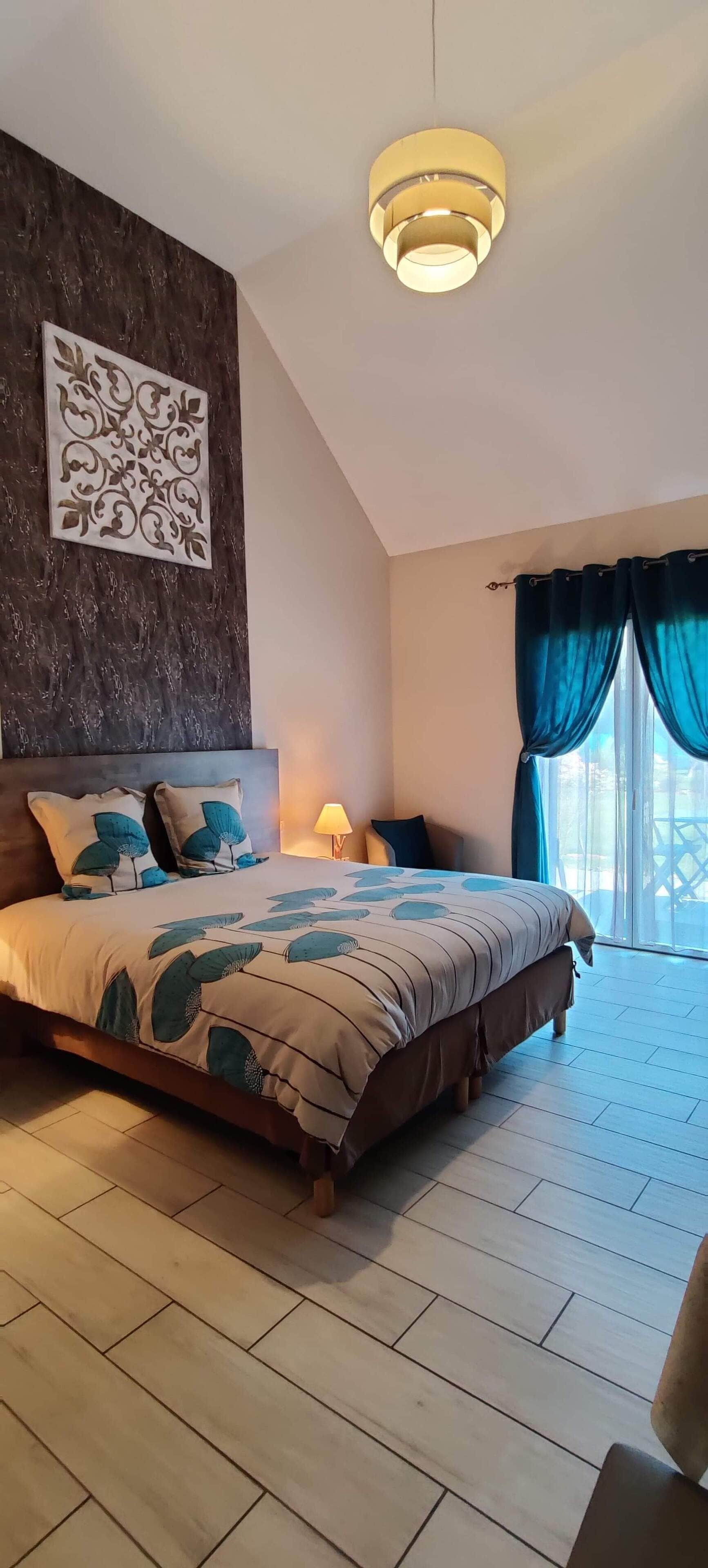 A bedroom with a large bed, a decorative wall piece, a ceiling light, and a view through a window with curtains.