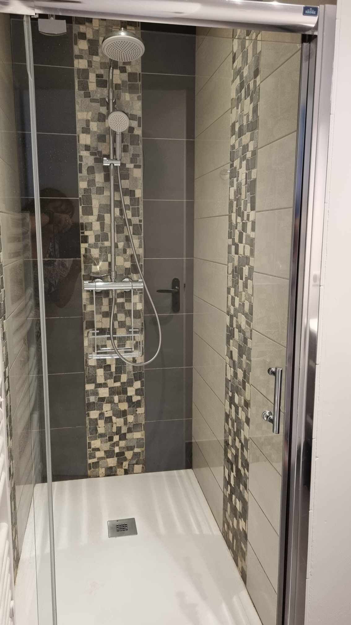 A walk-in shower with a glass door, tiled walls, and a showerhead.