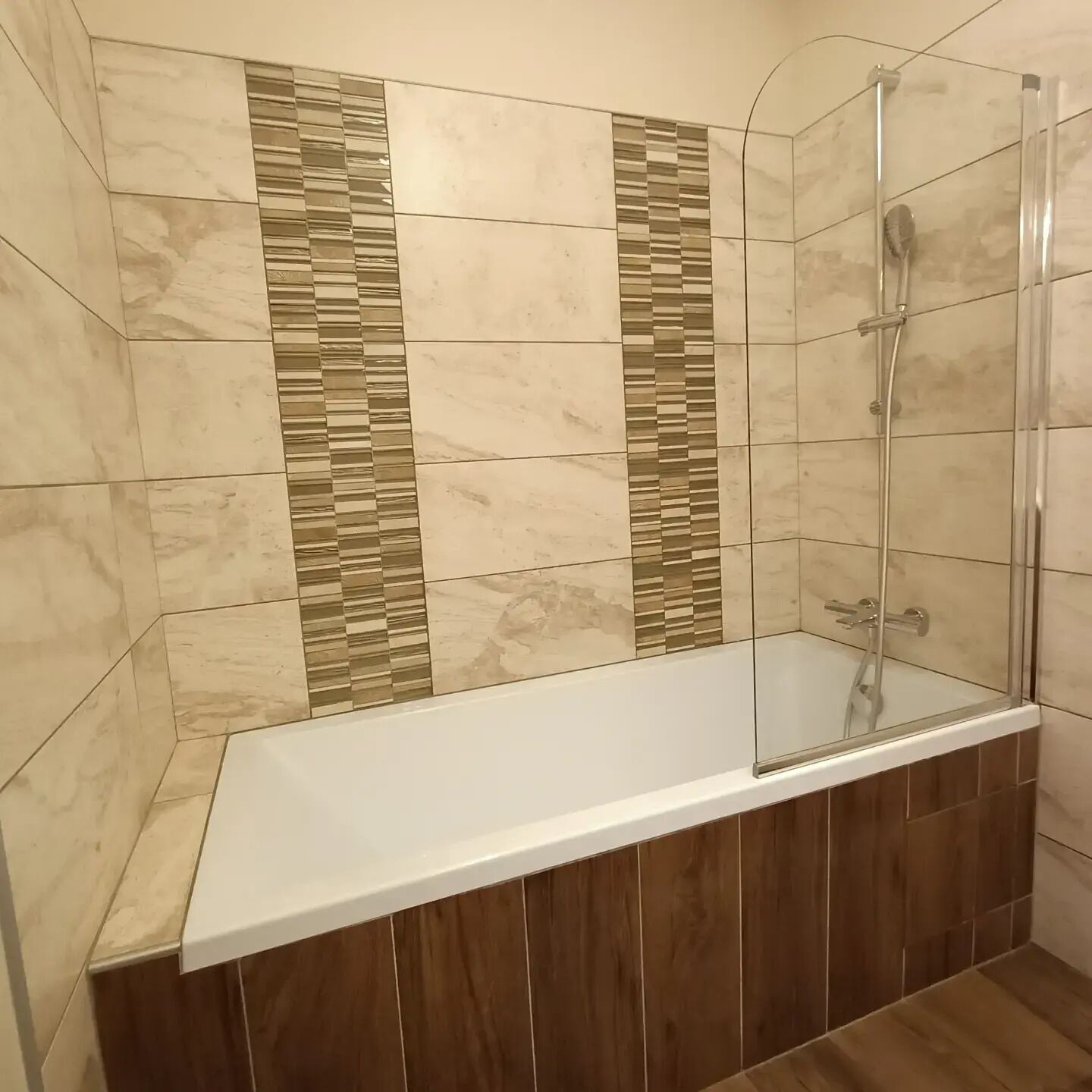 A modern bathroom with a glass-enclosed shower, a white bathtub, and a mix of beige and brown tiles.