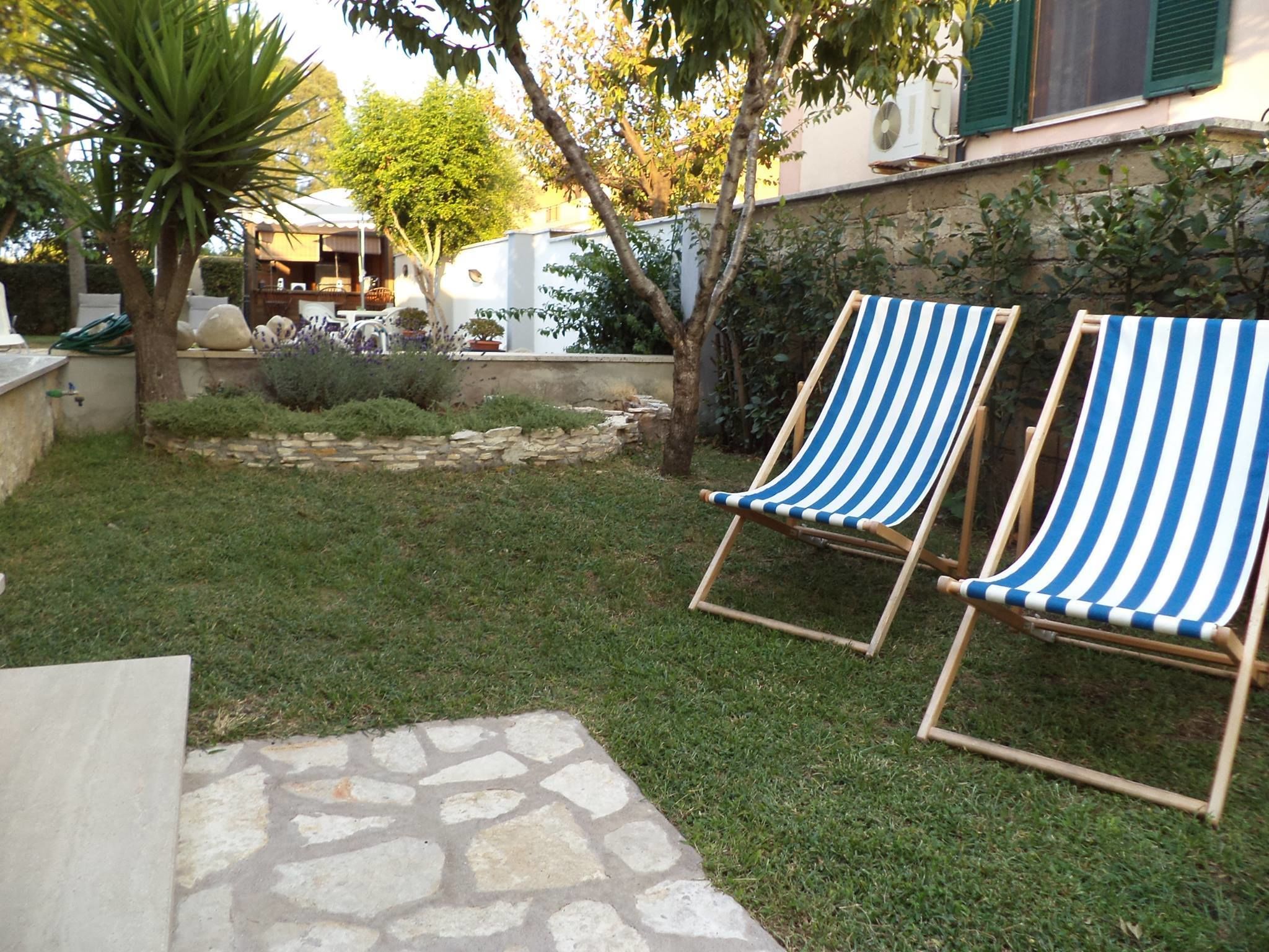 A garden with two striped lounge chairs, a stone pathway, and a small pool area.