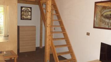 A room with a wooden staircase leading to a loft area, a small table, and a television on a stand.