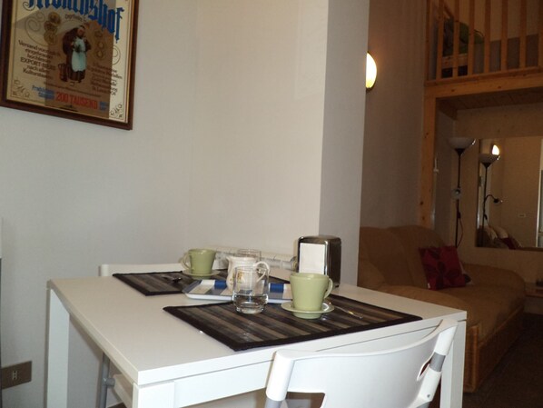 Un comedor con una mesa y sillas blancas, un cartel enmarcado en la pared y un techo de madera.