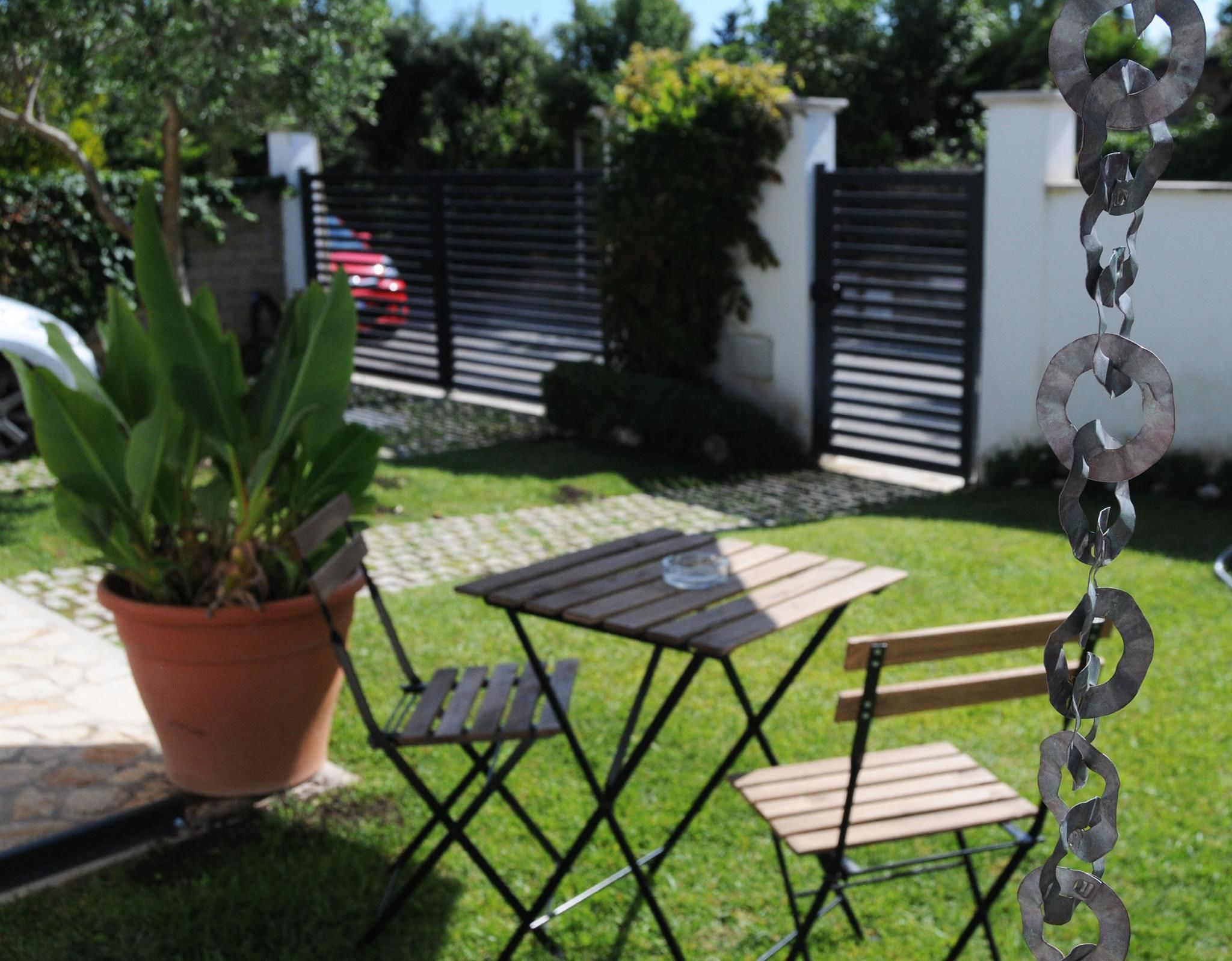 Un patio con una escultura de metal, una planta en maceta y una mesa con sillas.