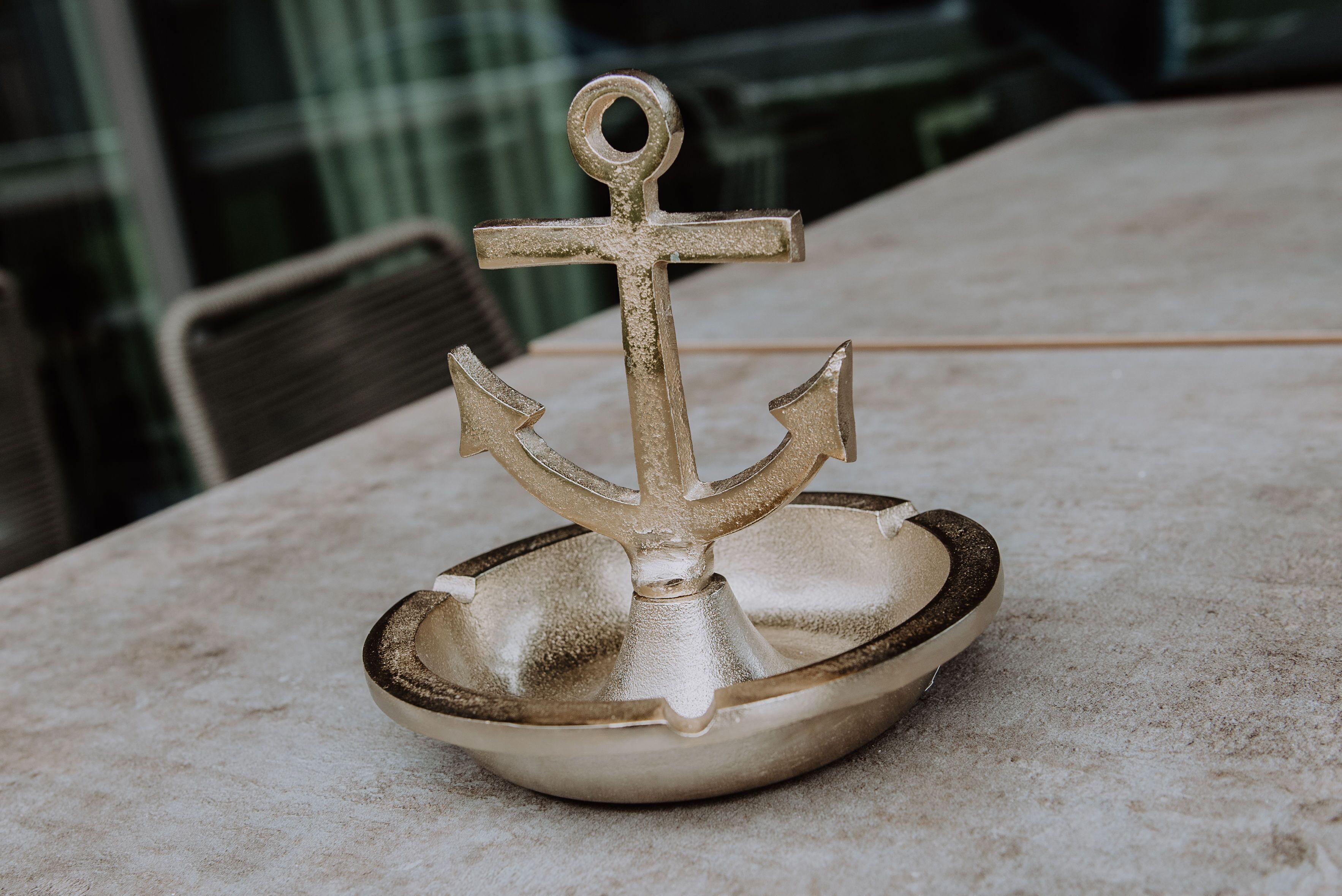 A brass anchor-shaped ashtray on a marble table.