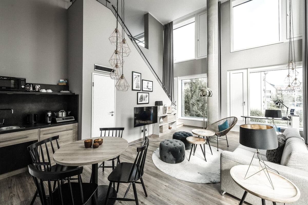Una cocina moderna con comedor, una sala de estar con sofá y otomanas, y un amplio ventanal con vista a la ciudad.